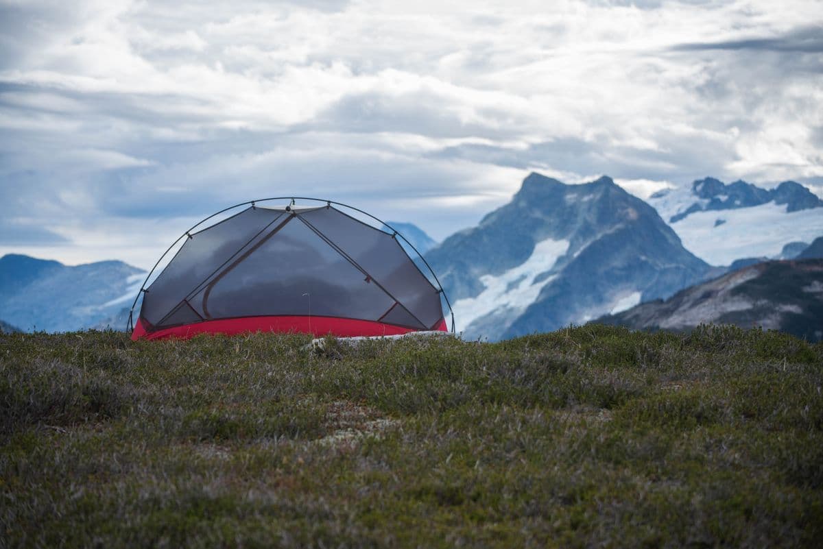 A dome tent below snowy mountain peaks